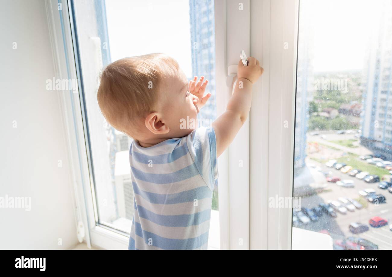 Bambino in pericolo. Baby boy tirando la maniglia della finestra Foto Stock