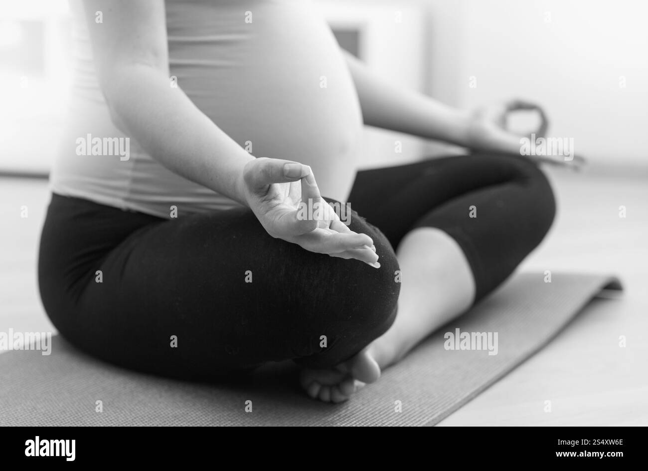 Closeup foto in bianco e nero della donna incinta a praticare yoga sul pavimento a casa Foto Stock
