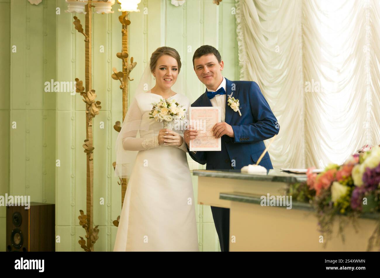 Ritratto di felice sposi novelli che pongono all ufficio del registro di sistema con contratto di matrimonio Foto Stock