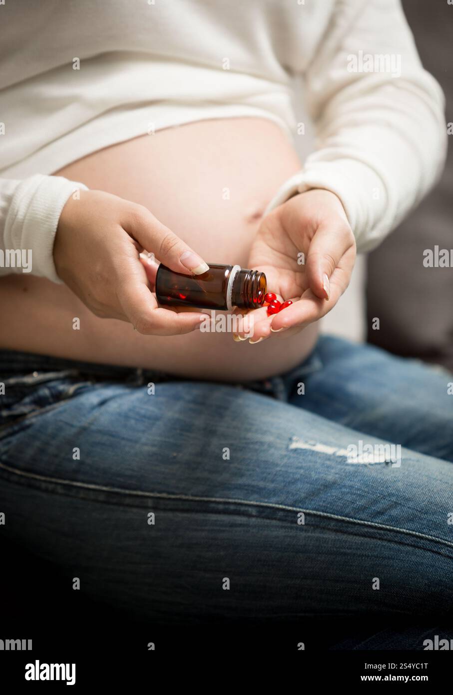 Donna incinta che prende vitamine in pillole dal flacone di vetro Foto Stock
