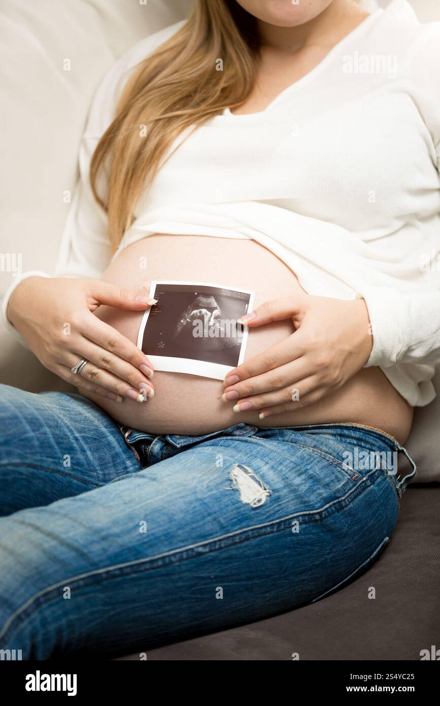 Foto ravvicinata di una donna incinta che posa con un'immagine ecografica a dimora Foto Stock