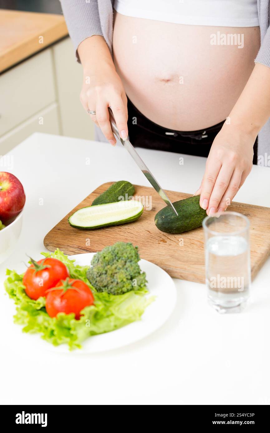 Foto ravvicinata di una donna incinta che prepara insalata di verdure in cucina Foto Stock