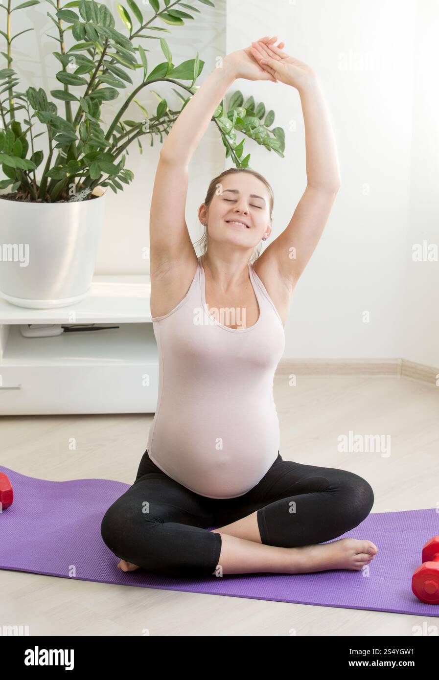 Giovane donna incinta che si allena sul tappetino per il fitness nel soggiorno Foto Stock