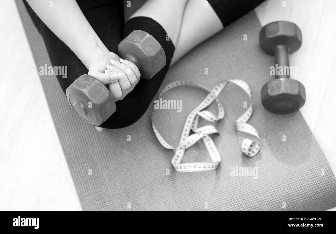 Foto in bianco e nero di una giovane donna seduta su un tappetino per il fitness e che solleva i manubri Foto Stock