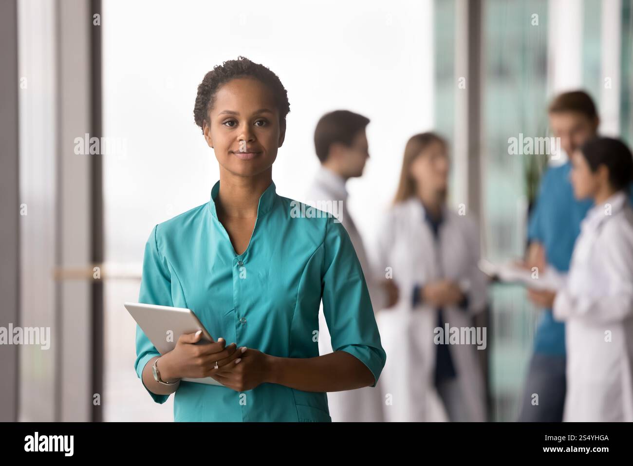 Donna africana medico che indossa scrub che posa in clinica con tablet Foto Stock