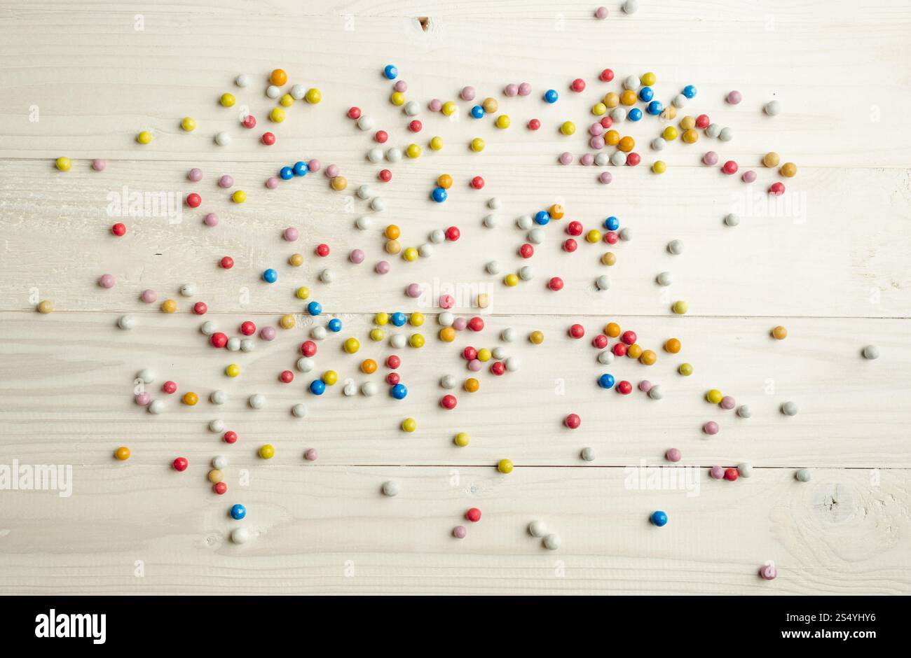 Caramelle rotonde colorate adagiate su tavole di legno bianche Foto Stock