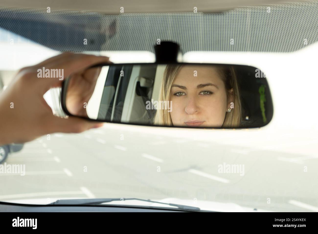 Primo piano di donna che regola lo specchio dell'auto e guarda nel riflesso Foto Stock