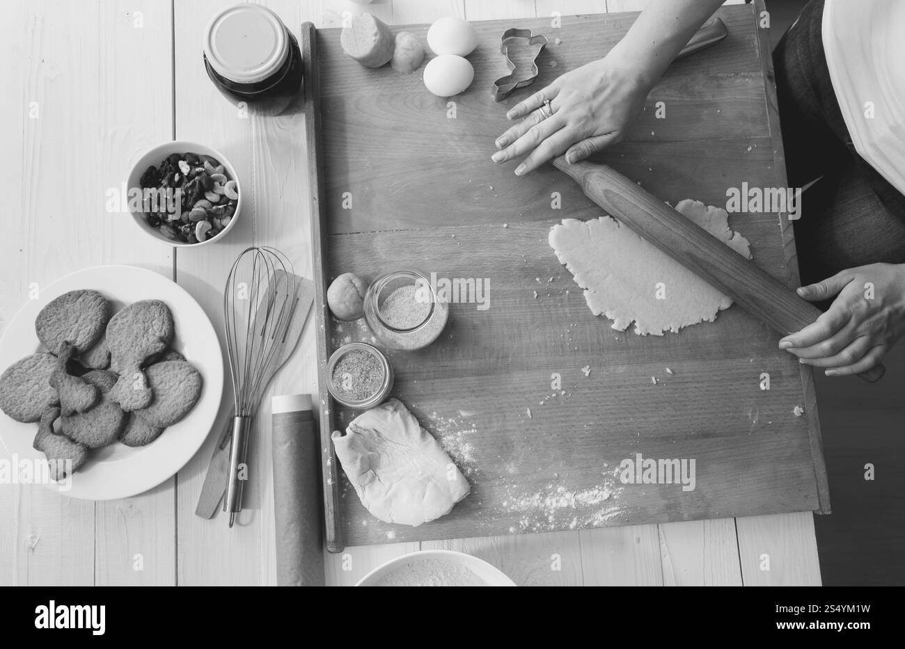 Foto in bianco e nero di una donna che prepara l'impasto per biscotti natalizi sulla scrivania di legno Foto Stock