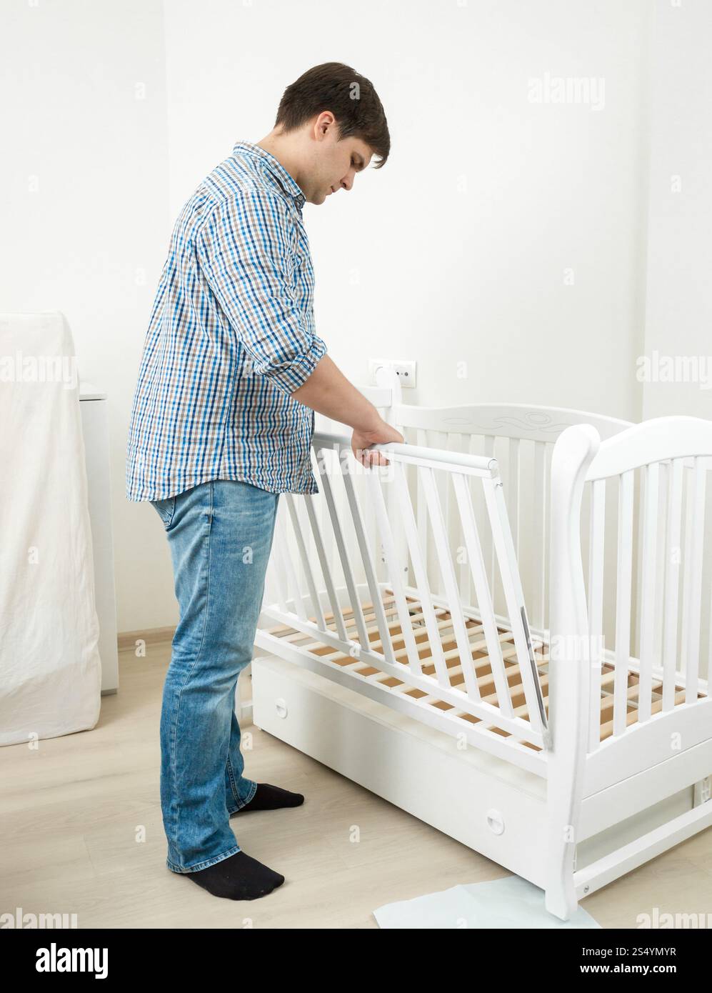 Bell'uomo in jeans e camicia che assembla un lettino per bambini Foto Stock