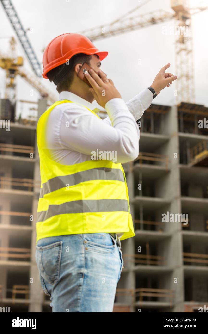 Un giovane uomo d'affari con elmetto e giubbotto di sicurezza che parla al telefono nel cantiere Foto Stock