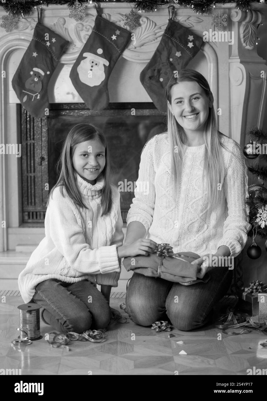 Immagine monocromatica della giovane madre e della figlia felici che confezionano regali di Natale sul pavimento del soggiorno Foto Stock