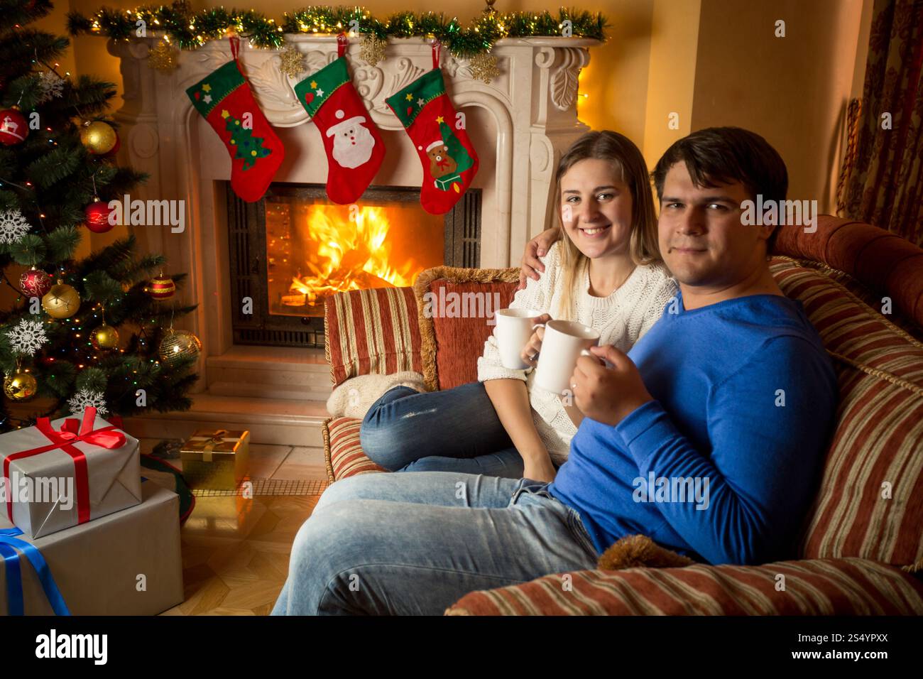 La giovane famiglia felice beve il tè sul divano al caminetto Foto Stock
