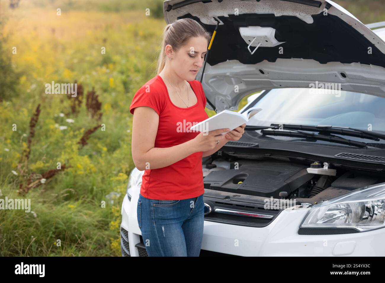 Donna che legge il manuale d'uso di un'auto rotta nel prato Foto Stock