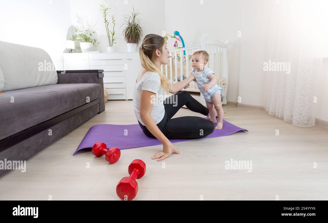 Bella madre sorridente con bambino che pratica yoga sul materassino in soggiorno Foto Stock