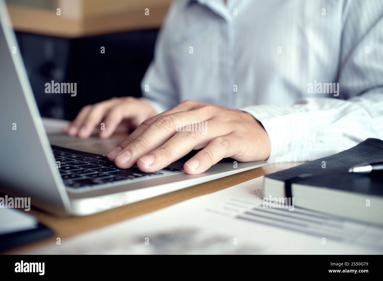 Uomo al lavoro utilizzando un computer portatile su un tavolo di legno. Mani digitando su una tastiera. Foto Stock