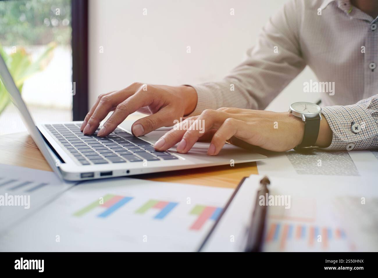 Uomo al lavoro utilizzando un computer portatile su un tavolo di legno. Mani digitando su una tastiera. Foto Stock