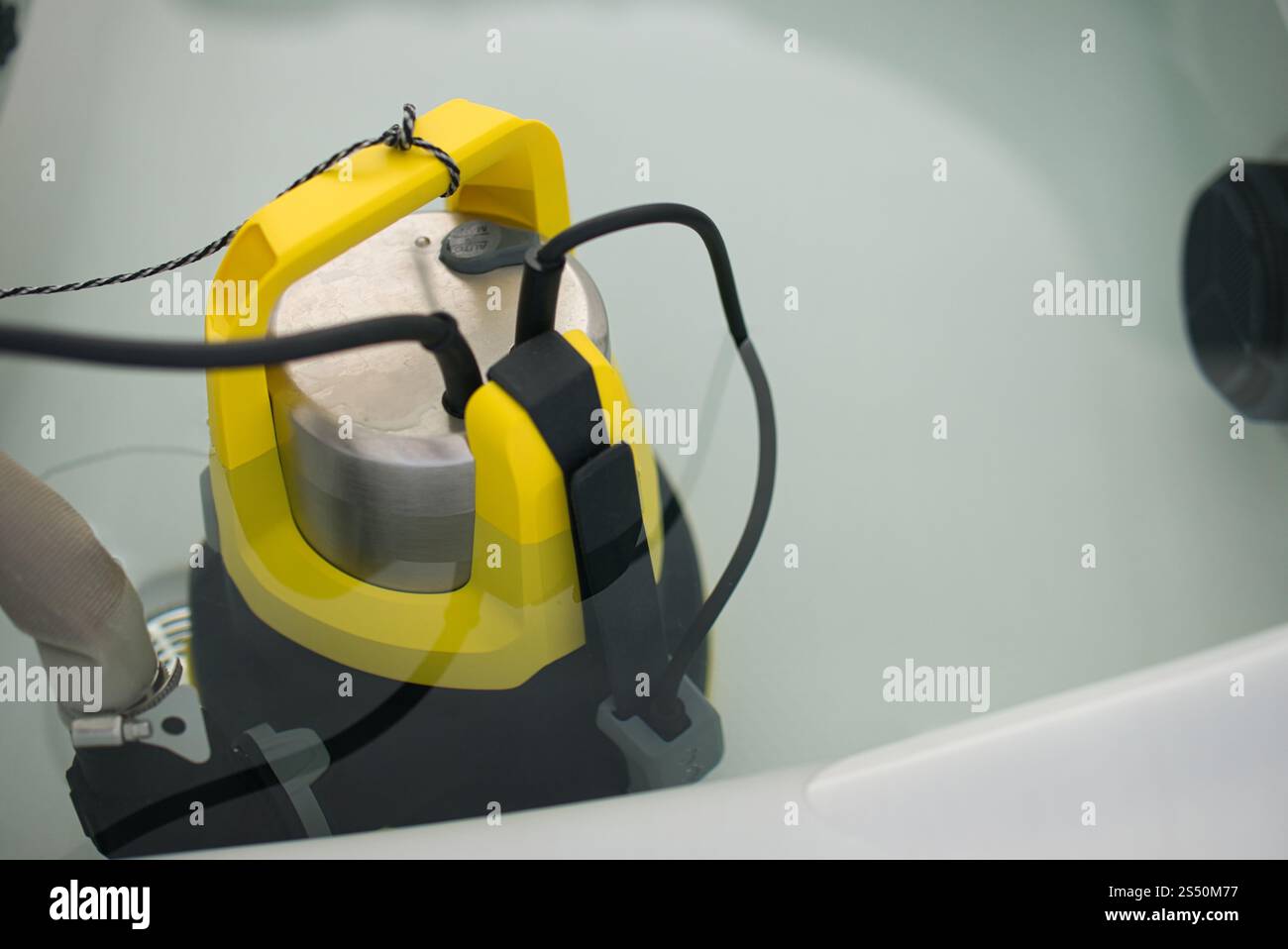 Pompa sommergibile in acciaio inox con manico giallo brillante e supporti per tubi in acqua idromassaggio. Concentrati sulla pompa. Filo collegato e cavo di alimentazione visibile Foto Stock