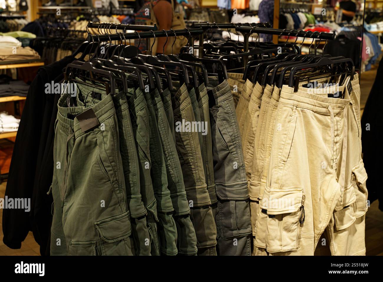 Una vivace gamma di pantaloncini cargo è appesa ordinatamente agli scaffali di un moderno negozio al dettaglio. Gli amanti dello shopping curiosano nelle vicinanze, creando un'atmosfera vivace piena di fas Foto Stock