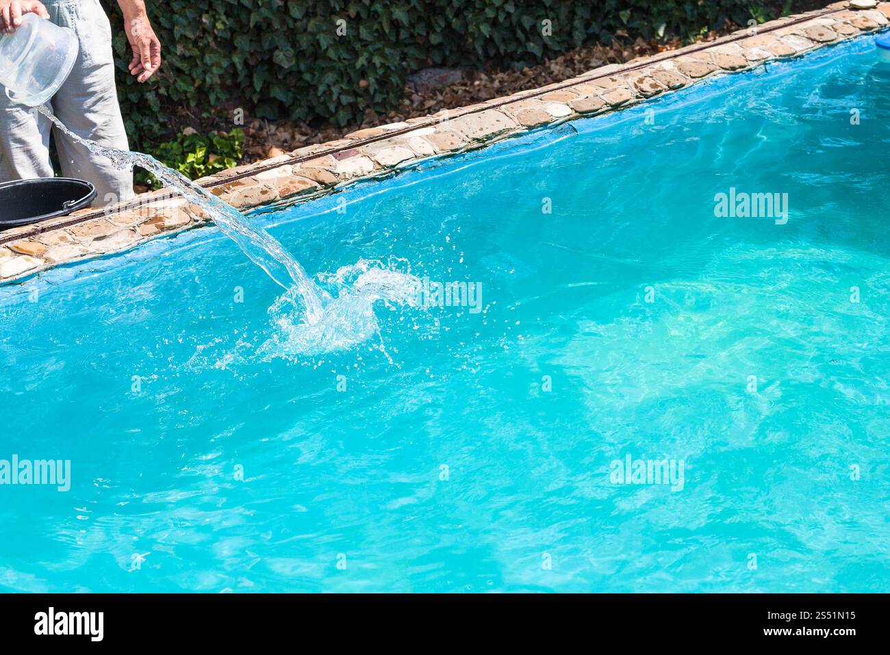 L uomo si riversa di disinfettante nella piscina esterna sul cortile della casa di paese Foto Stock