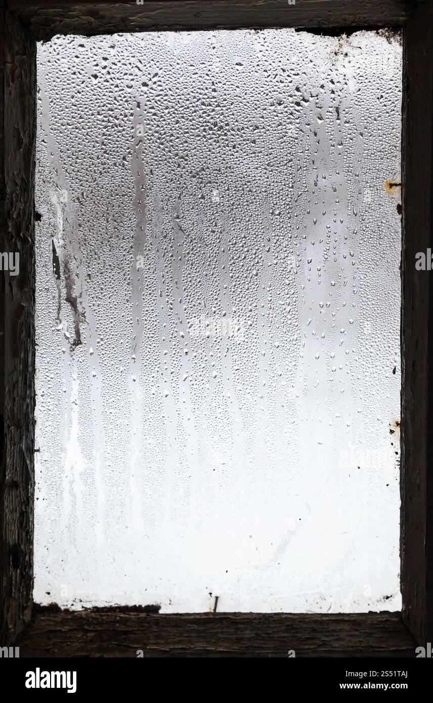 Gocce d'acqua dalla fusione della neve sulla superficie del vetro colmi in antica casa rurale in inverno Foto Stock