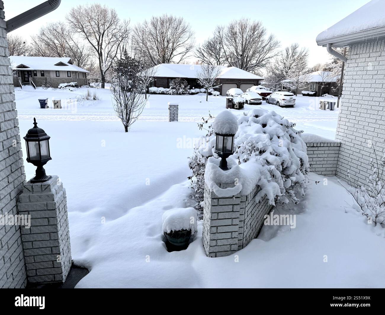 Neve pesante a Wichita, Kansas rivestito di oggetti e alberi. Mostra una strada residenziale e un quartiere e la parte anteriore di una casa con lampioni e pareti in mattoni. - Immagine stock catturata con smartphone