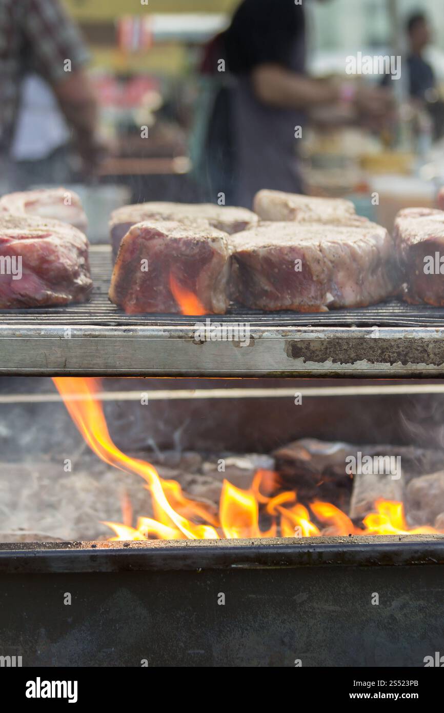 Primo piano di succose bistecche grigliate sulle fiamme aperte durante un evento di cucina Foto Stock