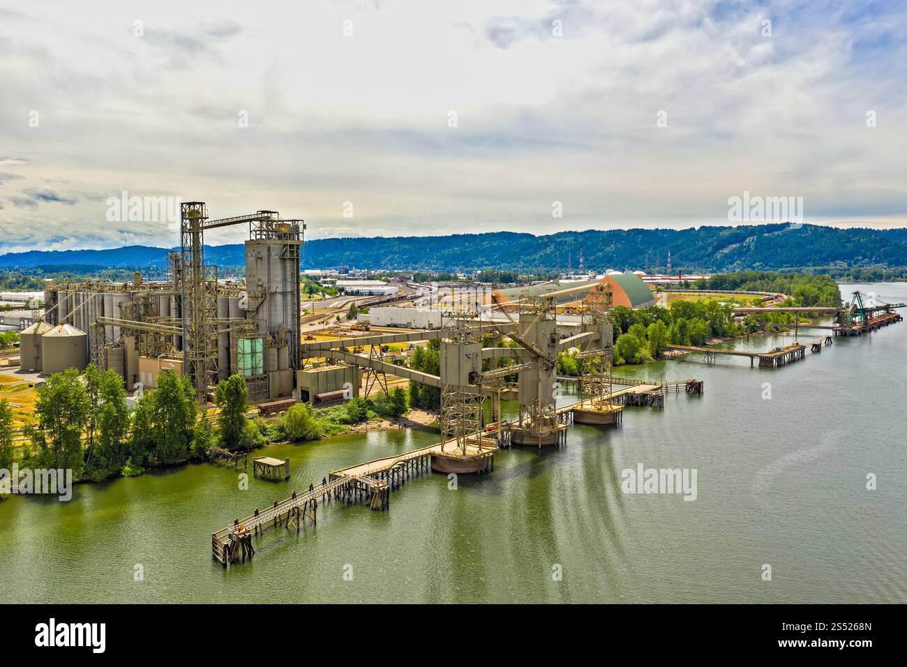 Impianto industriale sul lungomare con colline panoramiche sullo sfondo Foto Stock