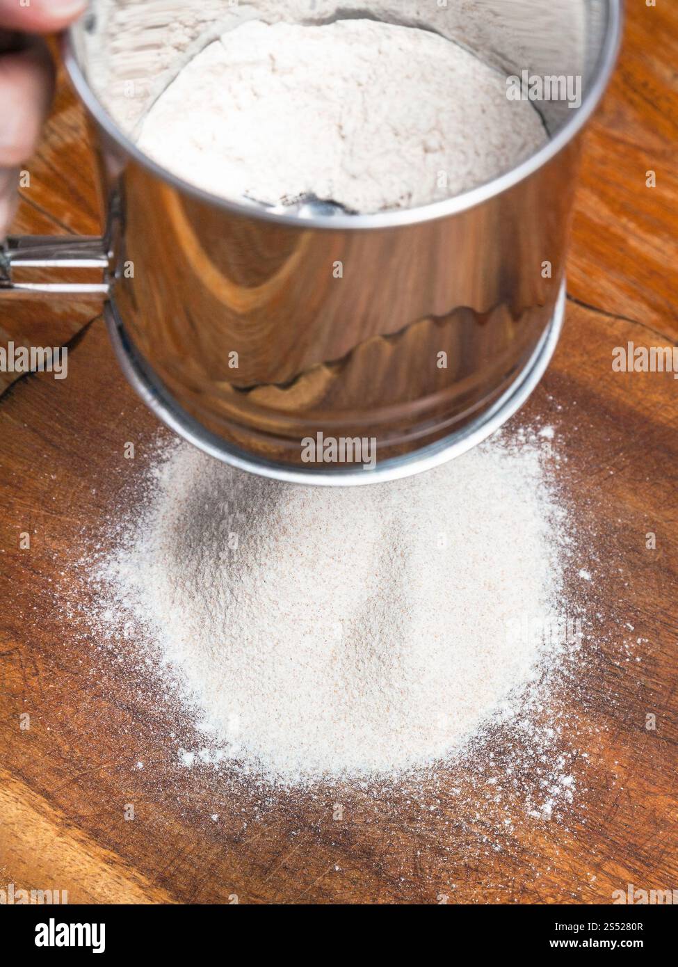 La cottura della torta - di setacciare la farina attraverso il setaccio in acciaio sul pannello di legno Foto Stock