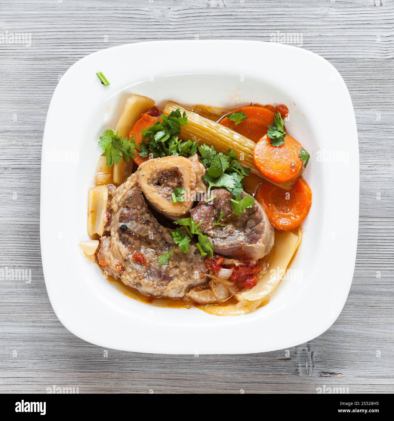 Vista superiore del piatto italiano Ossobuco in piastra bianca su grigio pannello di legno Foto Stock