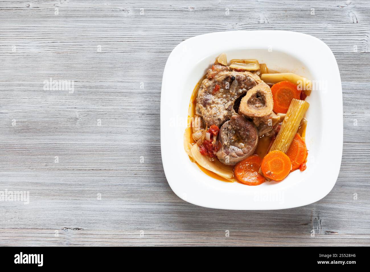 Vista superiore del cotto piatto italiano Ossobuco in piastra bianca su grigio asse di legno con copyspace vuoto Foto Stock