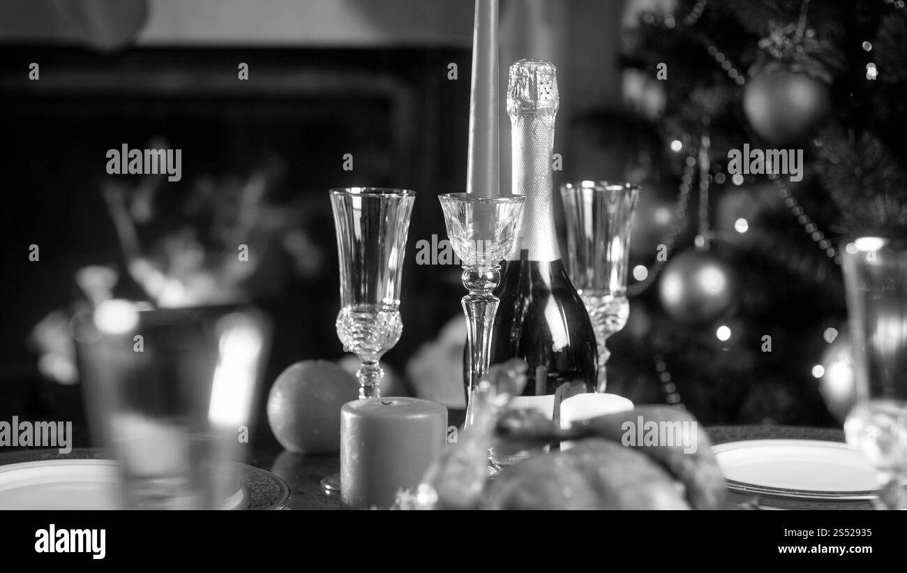 Foto in bianco e nero della bottiglia di champagne e dei bicchieri contro l'albero di Natale decorato. Immagine in bianco e nero della bottiglia di champagne e dei bicchieri contro Foto Stock