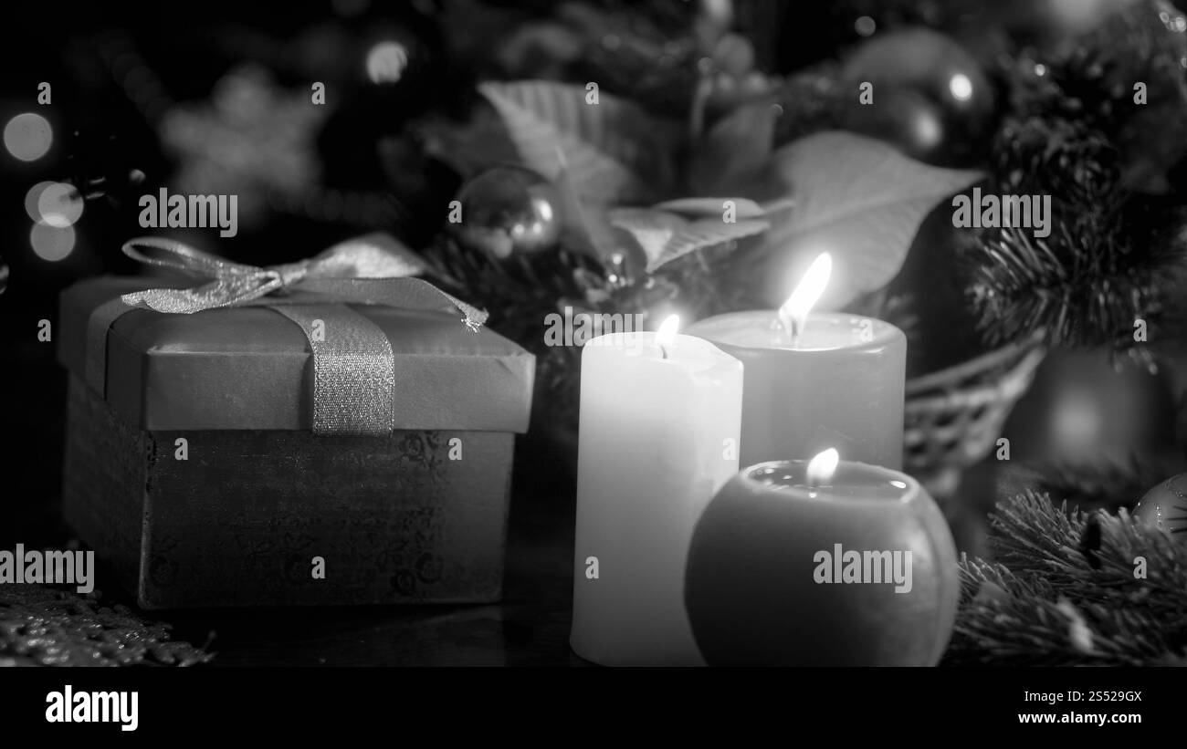 Foto in bianco e nero di tre candele bruciate e regali di Natale su sfondo di legno. Immagine in bianco e nero di tre candele in fiamme e Natale Foto Stock