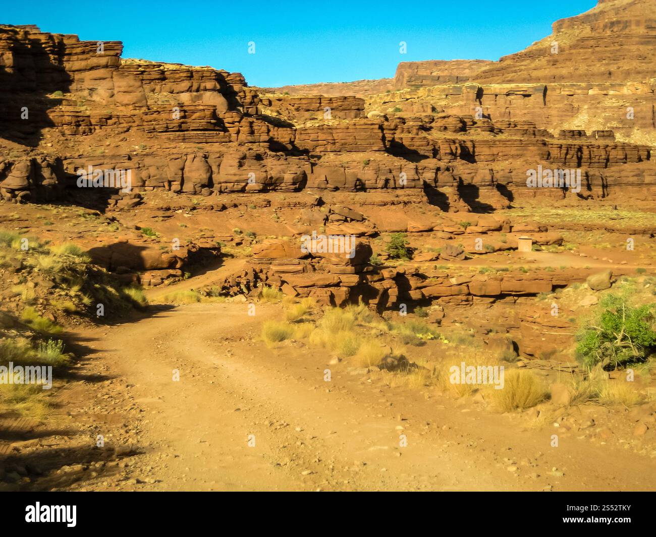 Una strada sterrata si snoda attraverso un canyon roccioso. La strada è stretta e tortuosa, e il canyon è pieno di rocce e massi. Il cielo è limpido e blu, e. Foto Stock