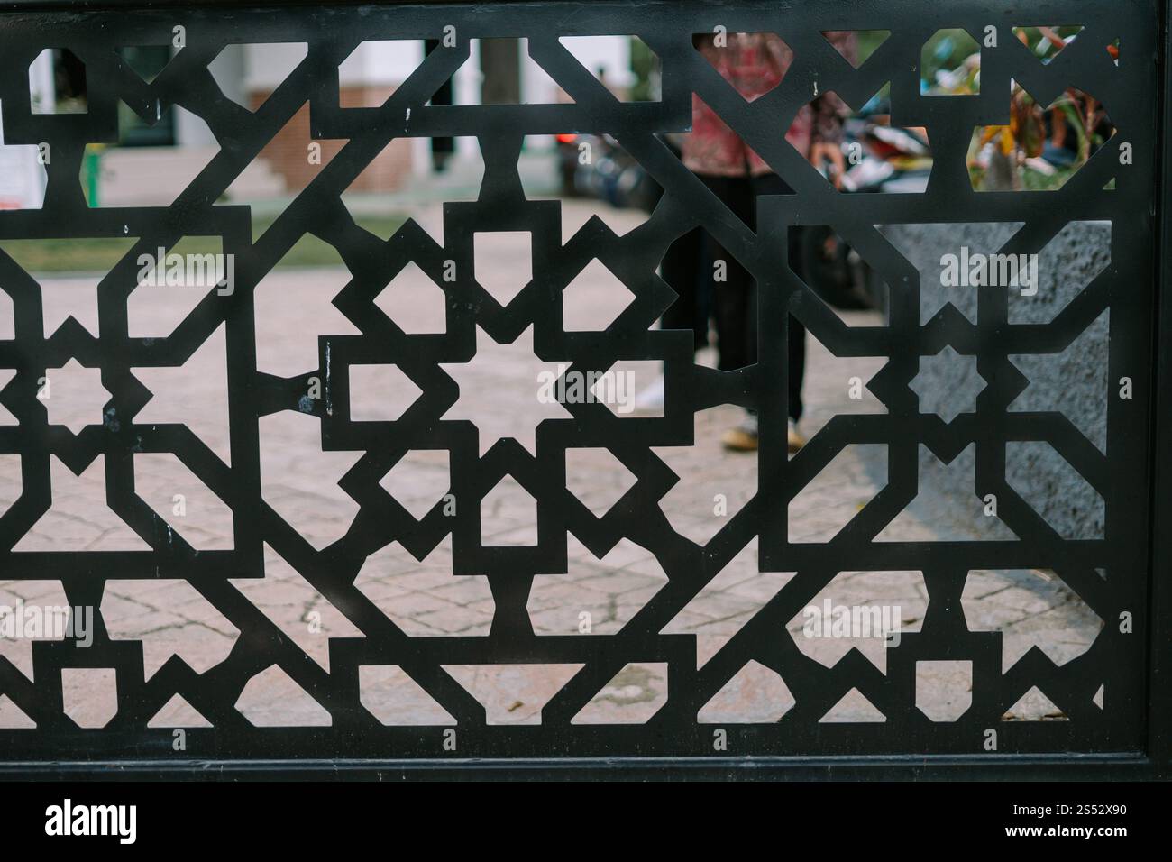 Intricato reticolo di metallo nero con motivi geometrici che danno un'occhiata a un cortile. Cattura un'estetica architettonica islamica. Foto Stock