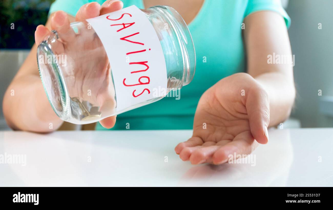Immagine ravvicinata di una giovane donna che svuota il vaso di vetro con poche monete. Foto ravvicinata di una giovane donna che svuota il vaso di vetro con poche monete Foto Stock