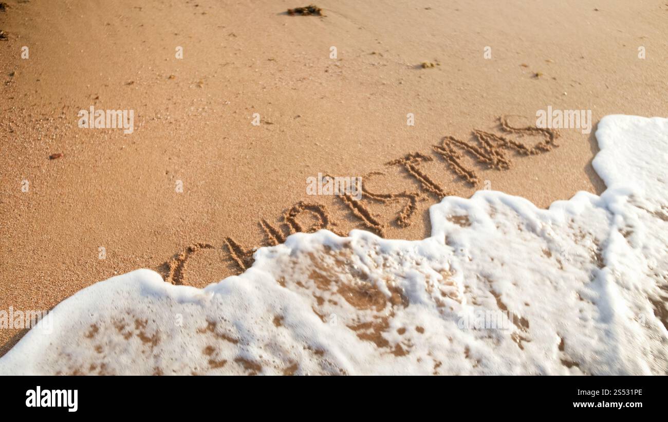 Immagine ravvicinata delle onde del mare che rotolano sopra la parola Natale scritta sulla sabbia bagnata. Concetto di vacanze invernali, Capodanno e turismo. Foto ravvicinata del mare Foto Stock