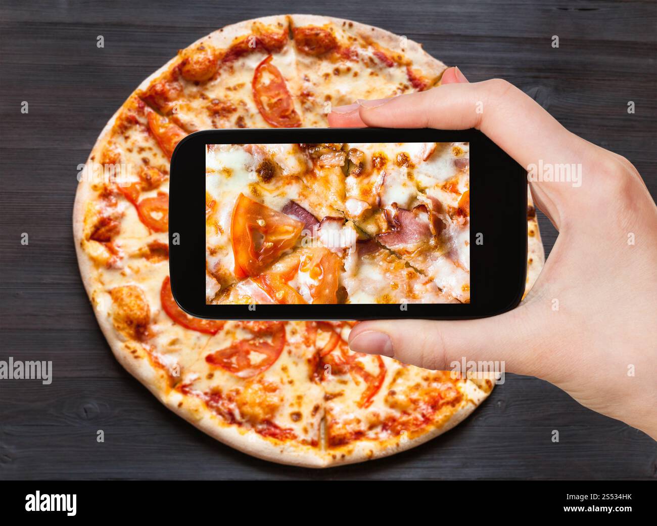 Concetto di viaggio - visitatore fotografie di riempimento di Pizza con pancetta e pomodori close up sullo smartphone Foto Stock