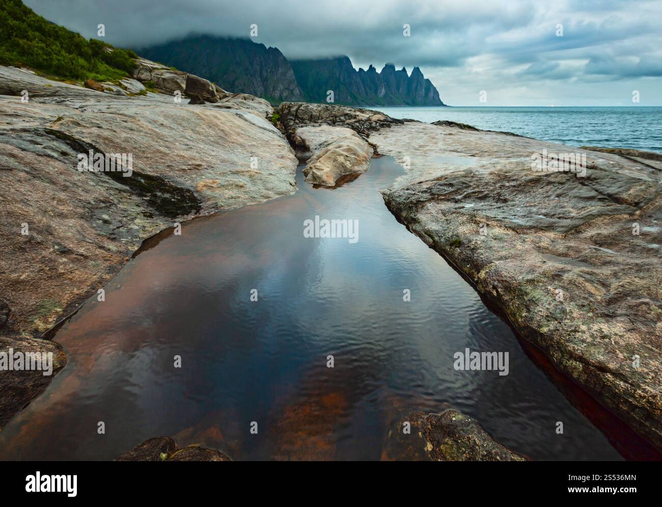 La spiaggia sassosa con bagni di marea a Ersfjord, Senja, Norvegia. Estate giorno polare notte costa. I denti di drago di roccia nel lontano. Foto Stock