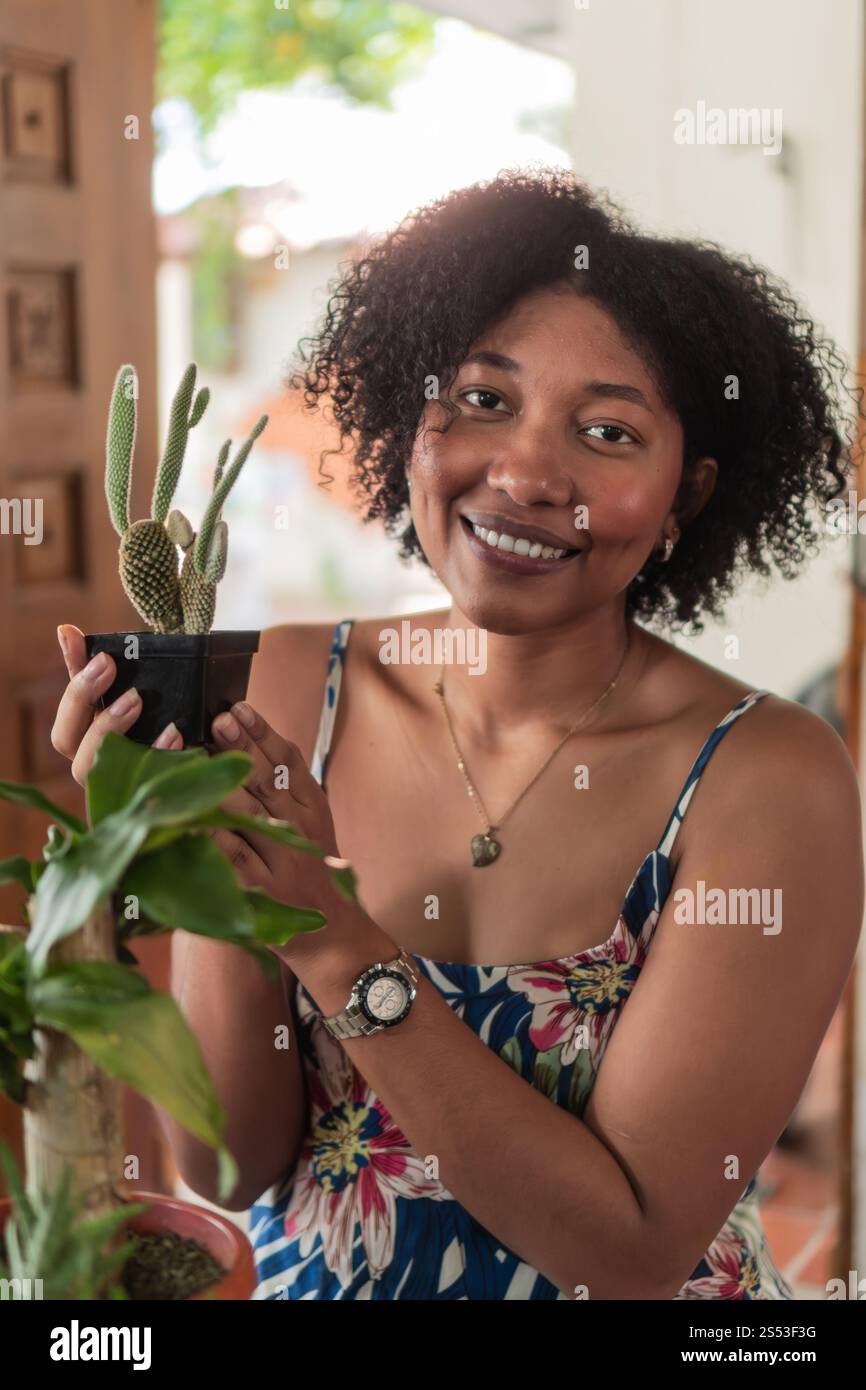 Giovane giardiniere che tiene in mano un piccolo vaso di cactus sorridente, piante da casa, vita domestica, etnia brasiliana Foto Stock