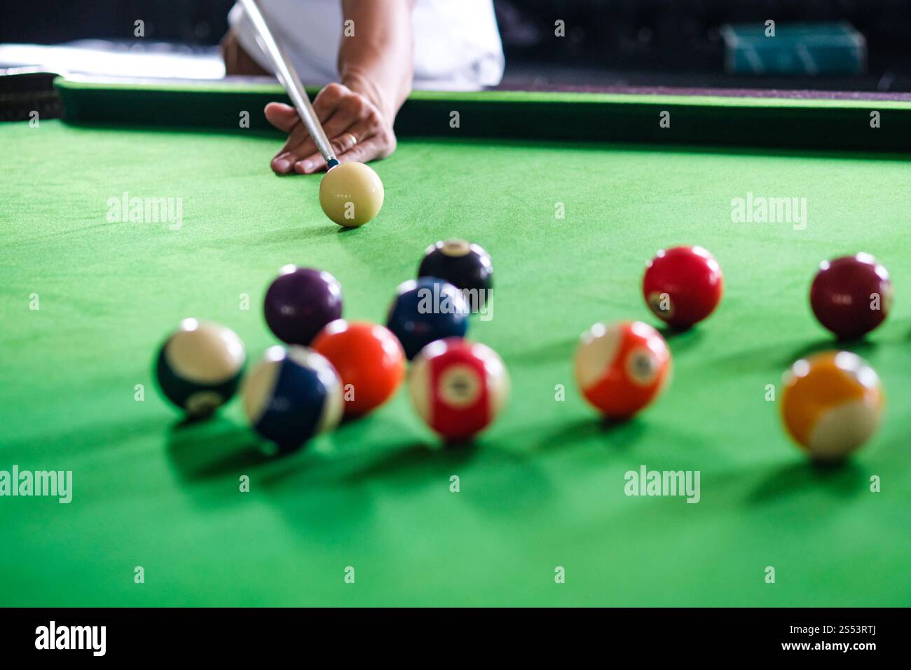 Mans mano e braccio cue giocano a biliardo o si preparano a sparare palle da biliardo su un tavolo da biliardo verde. Palline da biliardo colorate sul fregio verde Foto Stock