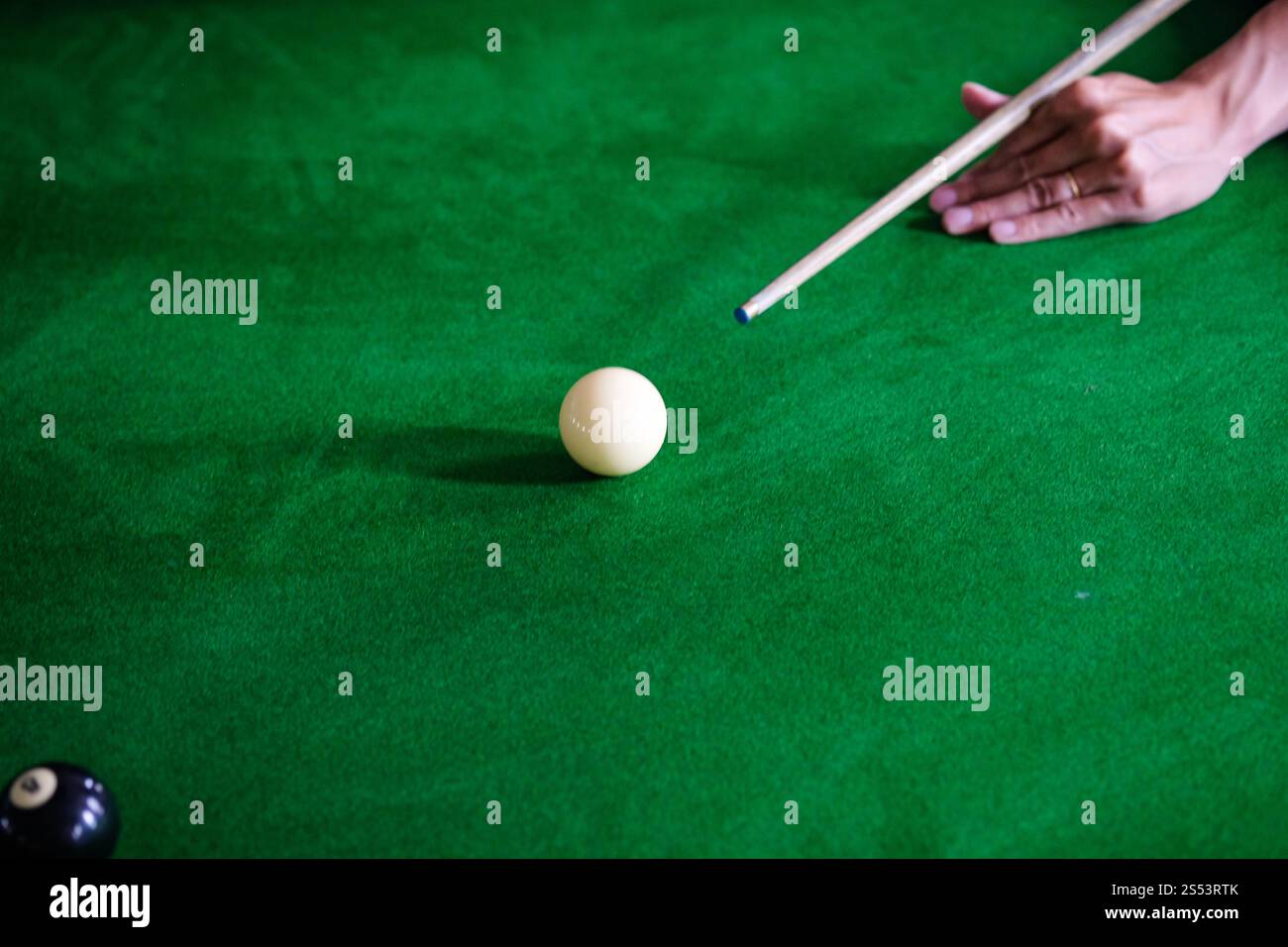 Mans mano e braccio cue giocano a biliardo o si preparano a sparare palle da biliardo su un tavolo da biliardo verde. Palline da biliardo colorate sul fregio verde Foto Stock