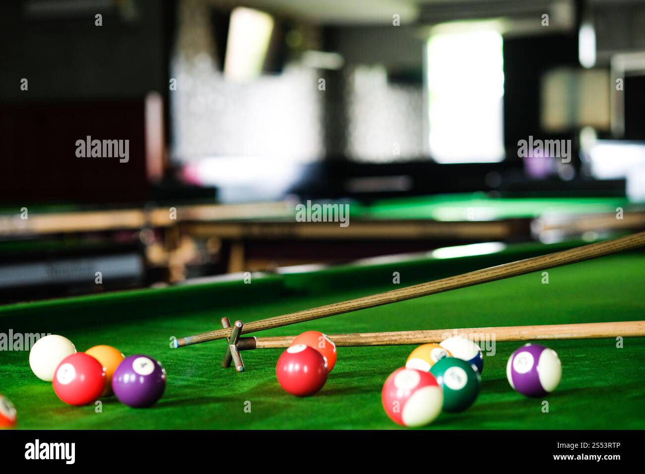 Mans mano e braccio cue giocano a biliardo o si preparano a sparare palle da biliardo su un tavolo da biliardo verde. Palline da biliardo colorate sul fregio verde Foto Stock