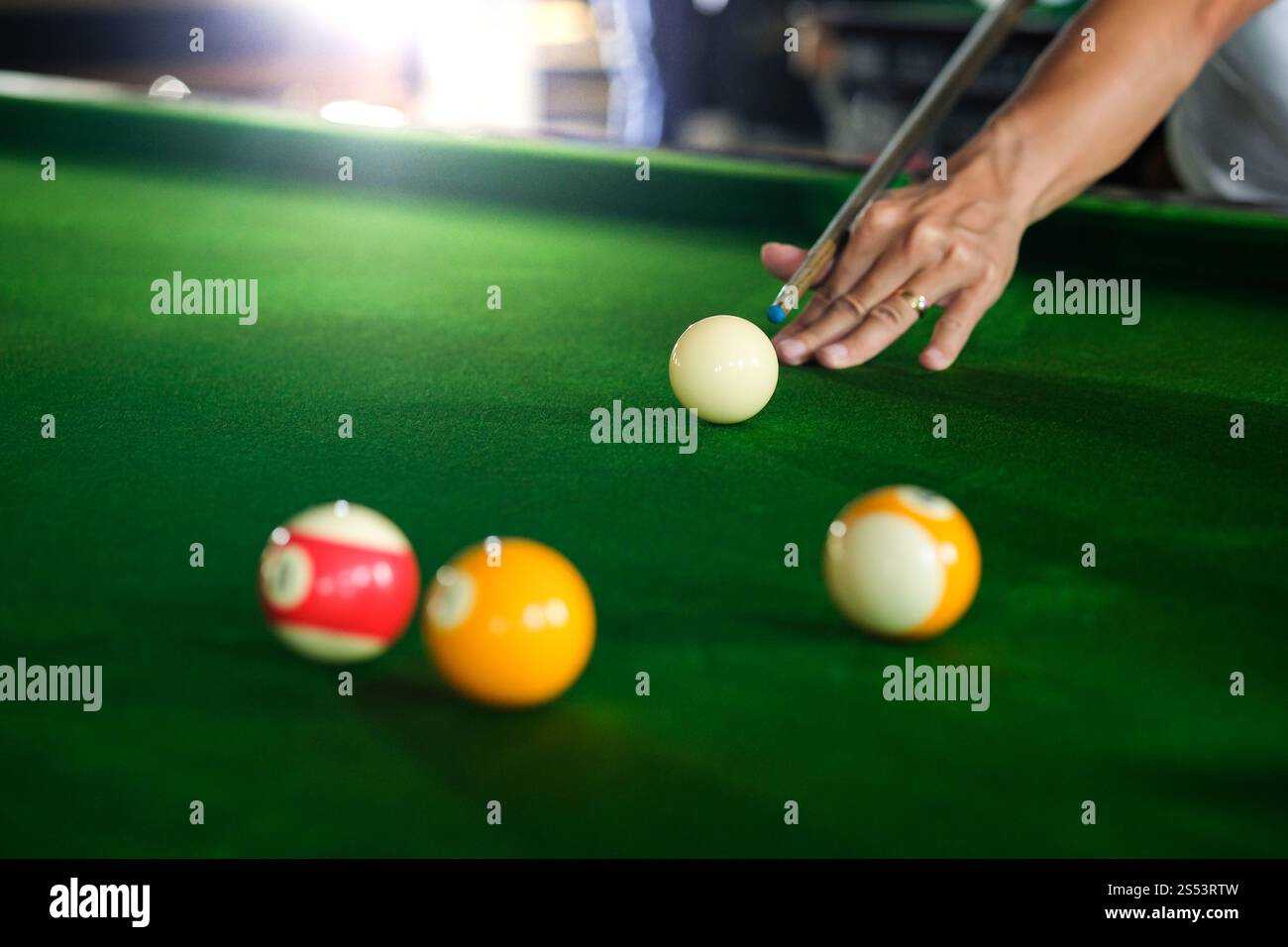 Mans mano e braccio cue giocano a biliardo o si preparano a sparare palle da biliardo su un tavolo da biliardo verde. Palline da biliardo colorate sul fregio verde Foto Stock