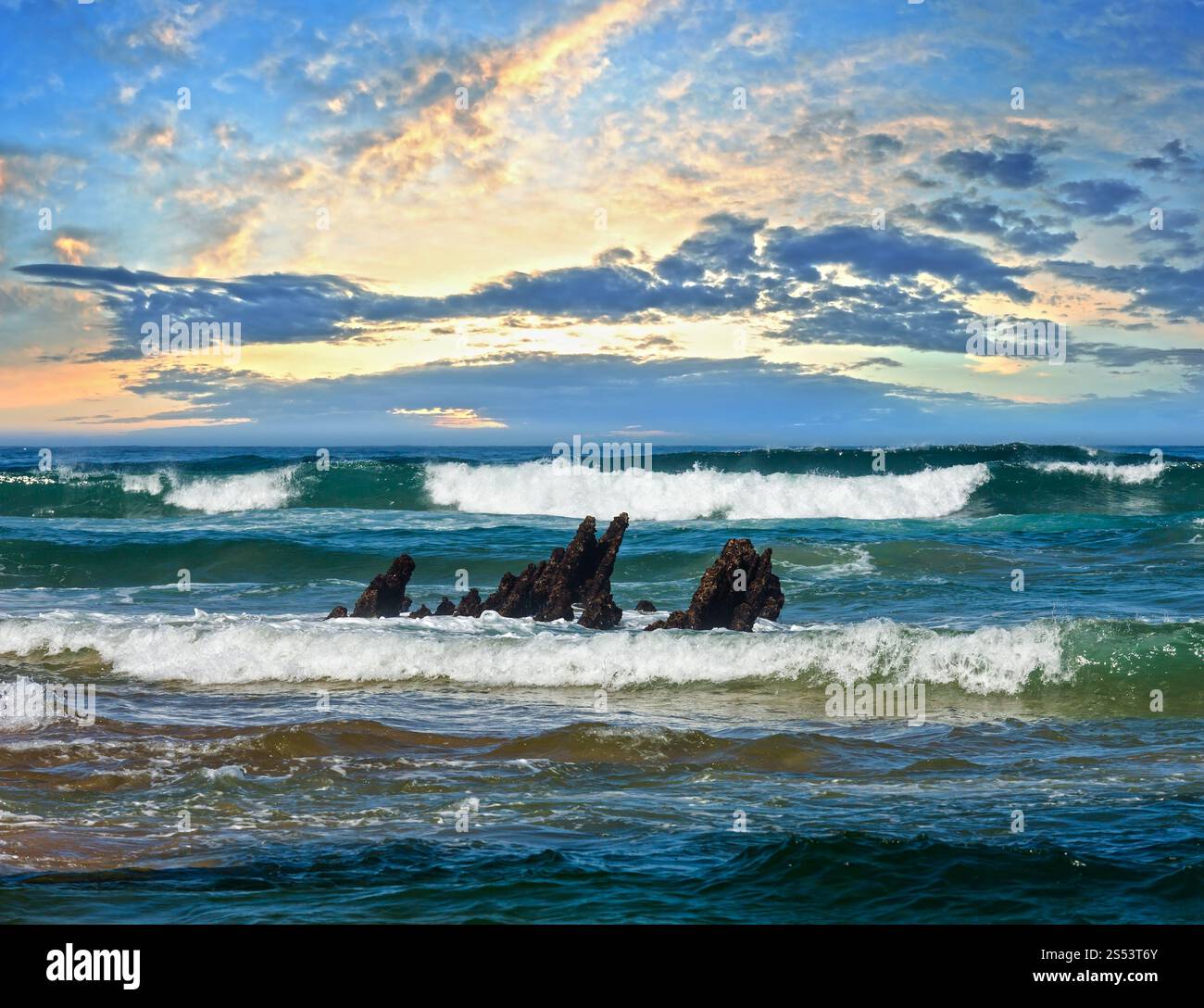 Mare onde da surf e piccole rocce in centro. Sera sunset seascape vista dalla spiaggia. Foto Stock