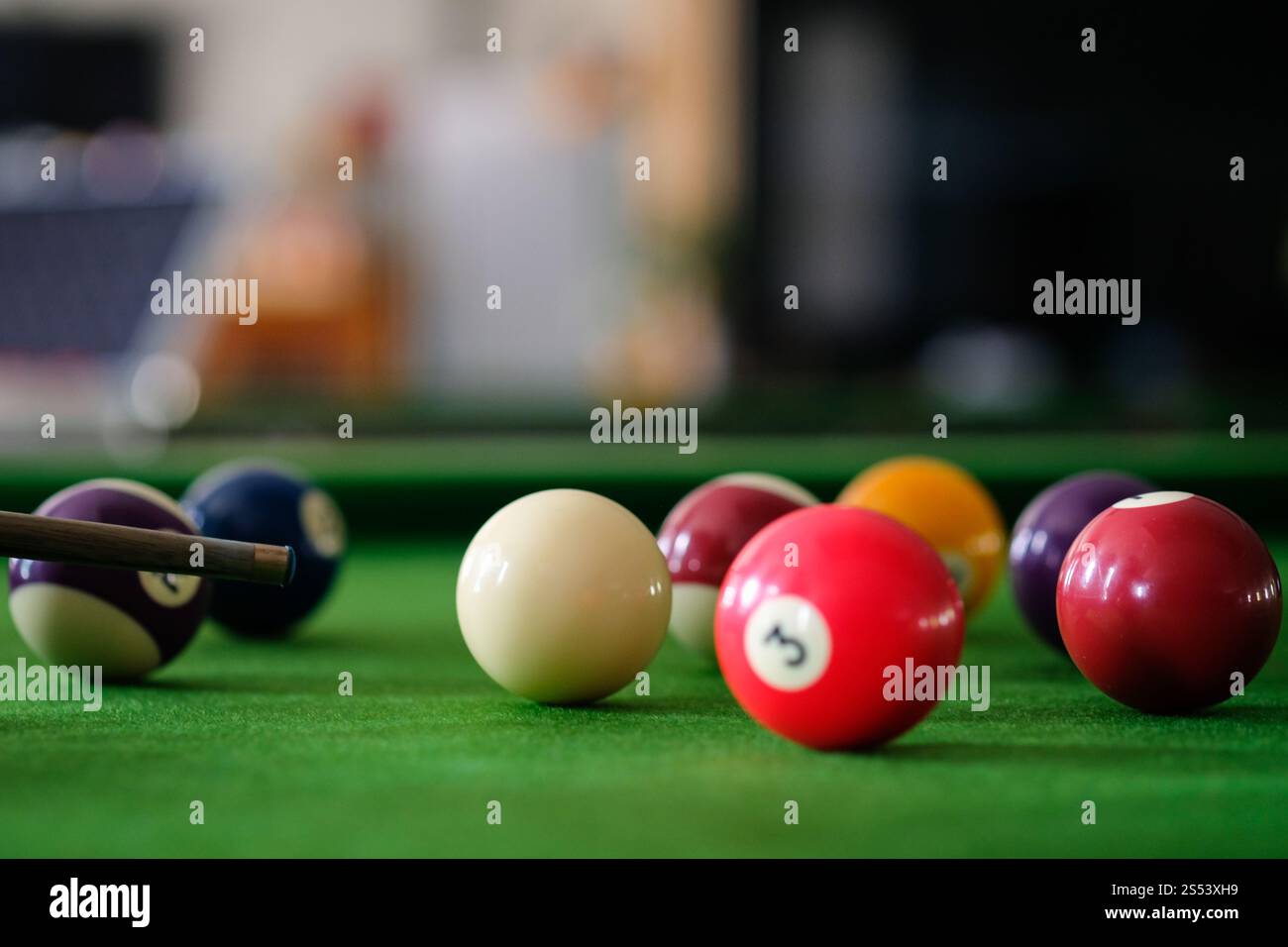 Mans mano e braccio cue giocano a biliardo o si preparano a sparare palle da biliardo su un tavolo da biliardo verde. Palline da biliardo colorate sul fregio verde Foto Stock