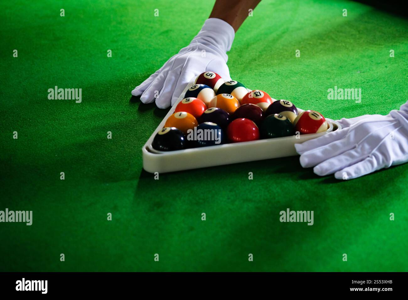 Mans mano e braccio cue giocano a biliardo o si preparano a sparare palle da biliardo su un tavolo da biliardo verde. Palline da biliardo colorate sul fregio verde Foto Stock