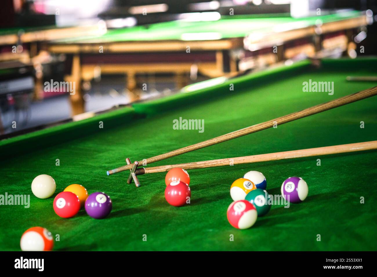 Mans mano e braccio cue giocano a biliardo o si preparano a sparare palle da biliardo su un tavolo da biliardo verde. Palline da biliardo colorate sul fregio verde Foto Stock