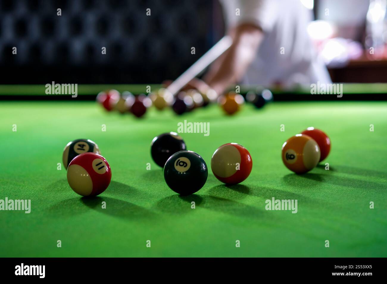 Mans mano e braccio cue giocano a biliardo o si preparano a sparare palle da biliardo su un tavolo da biliardo verde. Palline da biliardo colorate sul fregio verde Foto Stock