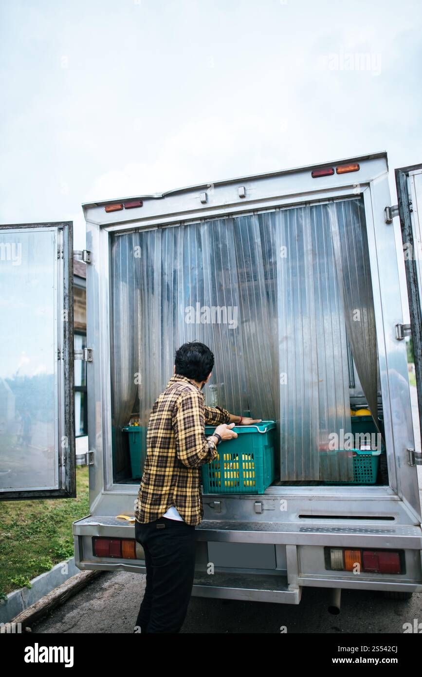 Ritratto di un agricoltore hipster che tiene la scatola di frutta sollevare fino alla macchina per andare mercato per la vendita. Foto Stock