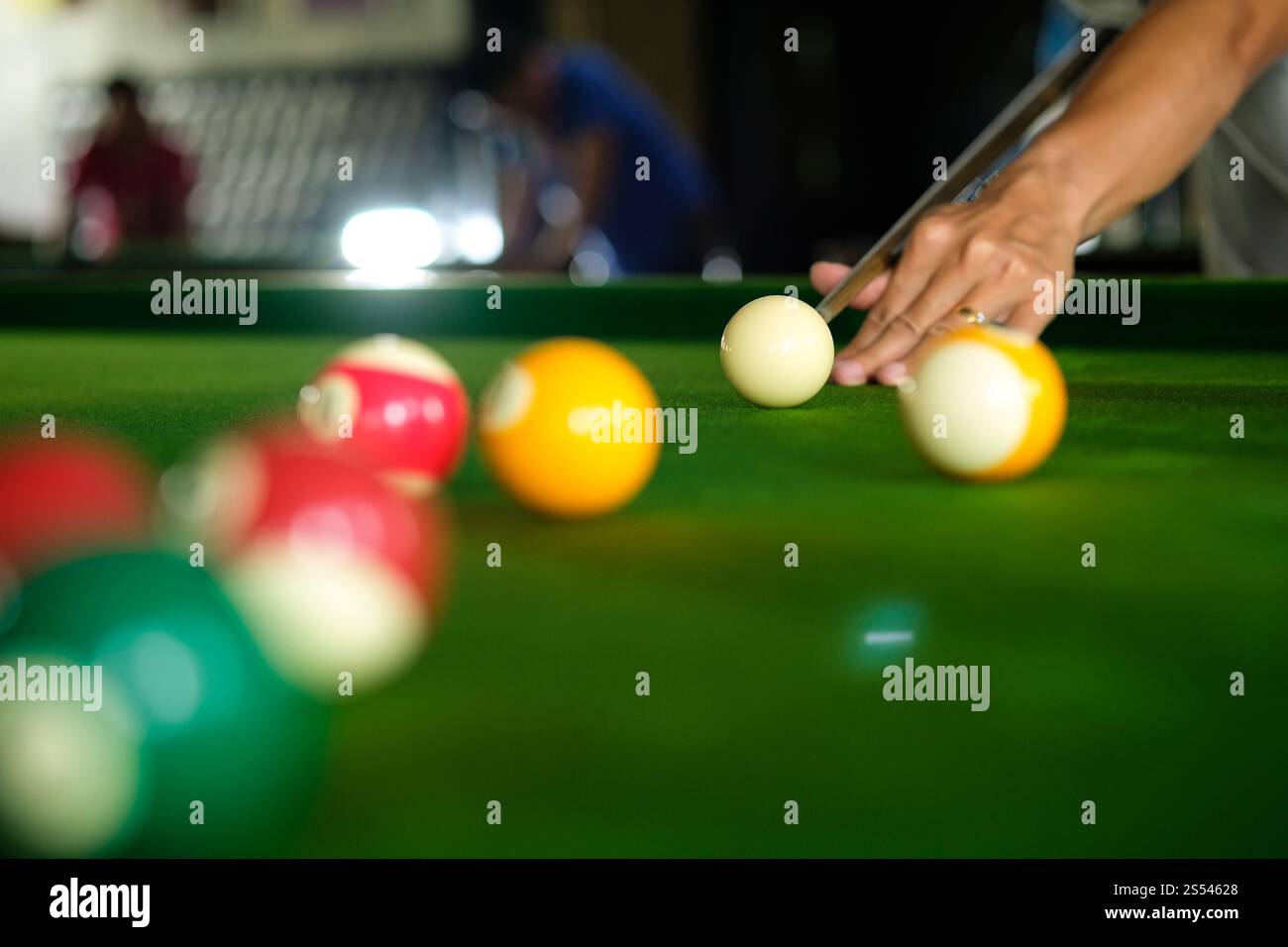 Mans mano e braccio cue giocano a biliardo o si preparano a sparare palle da biliardo su un tavolo da biliardo verde. Palline da biliardo colorate sul fregio verde Foto Stock
